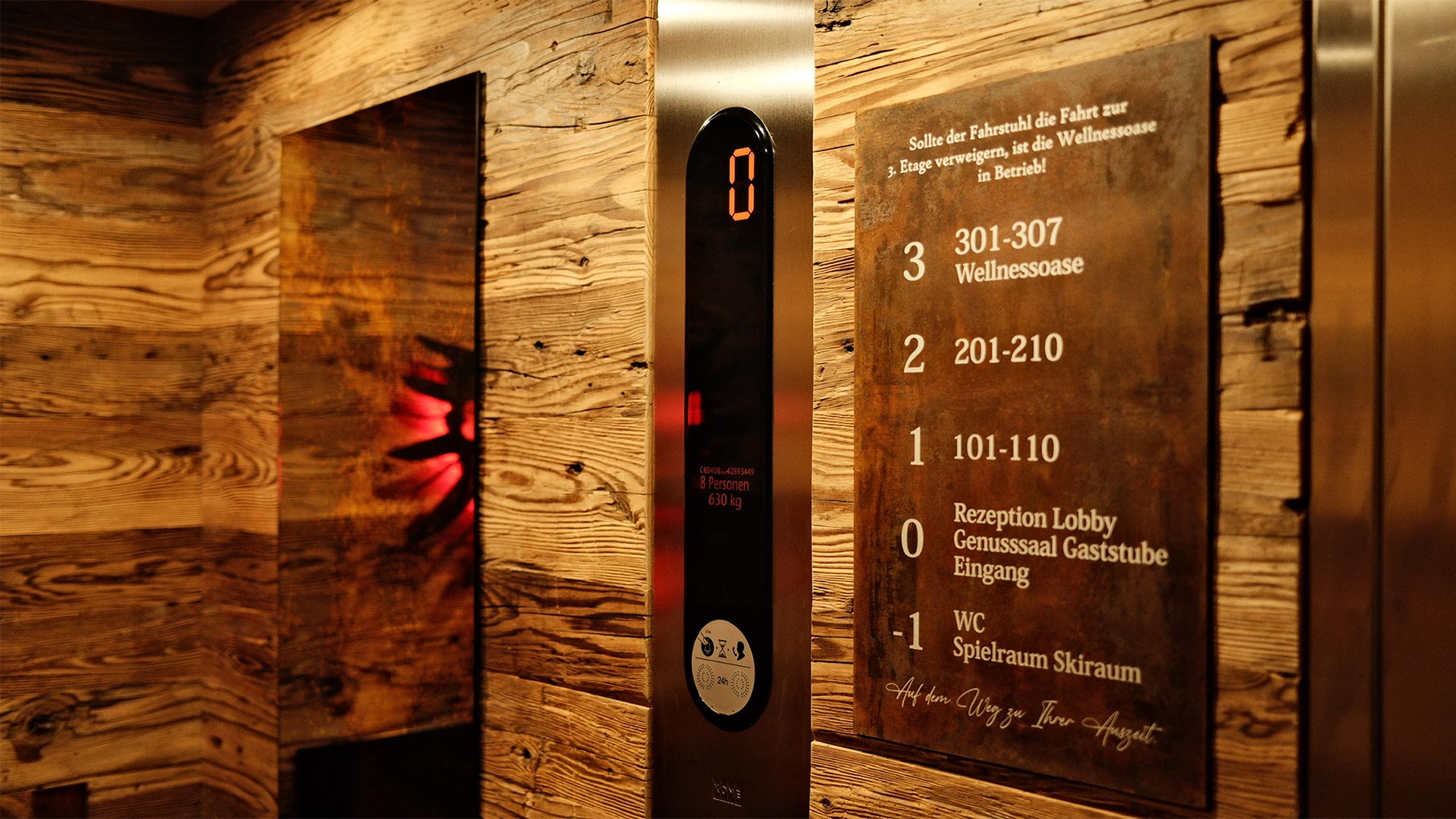 Holzverkleideter Aufzug mit digitaler Anzeige und Wegweiser zu Zimmern und Wellnessbereich
